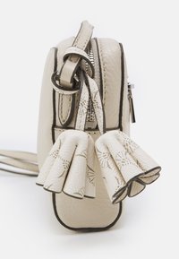 Krémová kožená kabelka s texturovaným povrchem, kovovým zipem a dvěma dekorativními třásněmi. Obsahuje tmavé okraje a popruh přes tělo.