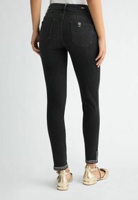 Jeans skinny neri con un design elegante, caratterizzati da dettagli in metallo argentato alla caviglia e tasche posteriori standard. Abbinati a ballerine dorate.