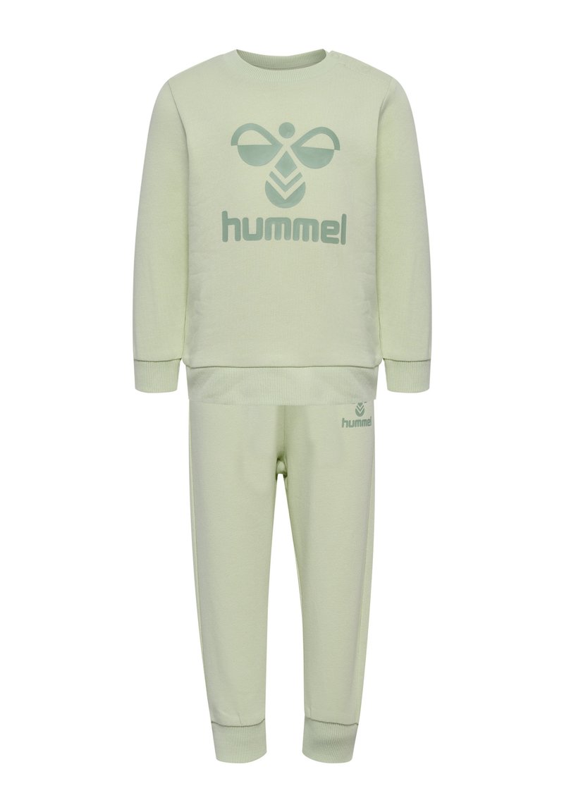 Jasnozielony zestaw z dresu, składający się z bluzy i spodni, z dużym logo "hummel" w ciemniejszym zielonym kolorze. Wykonany z miękkiego materiału, z ściągaczami przy mankietach i w pasie.