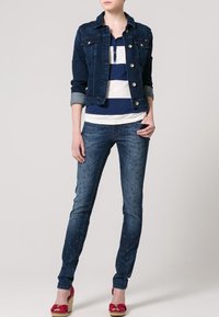 Jeansjacka i mörkblått med två bröstfickor; vit och marinblå randig skjorta; åtsittande blå jeans med stjärnmönster; röda kilklackar.