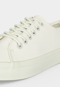 Hvid lav-top sneaker med hvide snørebånd trådte gennem seks metaløjer på hver side og en tyk hvid gummisål.