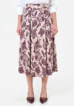 Femme portant une jupe midi beige imprimée de fleurs violet foncé, associée à un chemisier blanc et des talons pointus violet foncé.