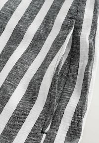 Tissu à rayures noires et blanches avec un tissage texturé. Les rayures varient en largeur et sont régulièrement espacées, créant un motif sur le matériau.