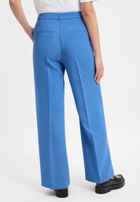 Blauwe wijde broek met een soepele textuur, voorzien van twee achterzakken en een getailleerde pasvorm, gecombineerd met zwarte plateau-schoenen.