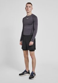 Herre træningsoutfit bestående af en grå langærmet skjorte og sorte shorts. Skjorten er tætsiddende, mens shortsene har en løs pasform og sideslidser.