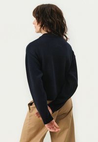 Navy blue knitted sweater with a ribbed round neck and cropped length. Features dropped shoulders and a textured finish.