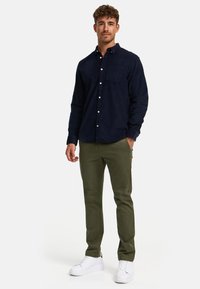 Marinblå kordkrage skjorta, olivgröna byxor och vita sneakers. Skjortan har en bröstficka och en avslappnad passform.