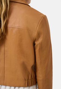 Brun læderjakke med en cropped design, let glans og elastisk talje. Har synlige sømme og en skræddersyet krave.