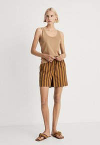 Een tan mouwloos topje gecombineerd met bruin en oranje verticaal gestreepte shorts. De shorts hebben een gestrikt tailleband. Platte sandalen met geknoopte banden.