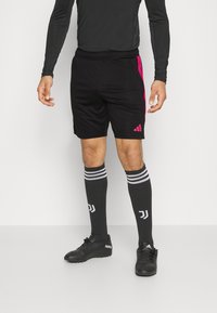 Pantalones cortos deportivos negros con detalles en rosa, combinados con calcetas negras hasta la rodilla con rayas blancas y logotipo, y botas de fútbol negras.