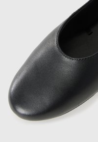 Zwarte leren platte schoen met een ronde neus, een gladde textuur en een eenvoudig ontwerp. Het interieur is donker, met minimale stikseldetails.