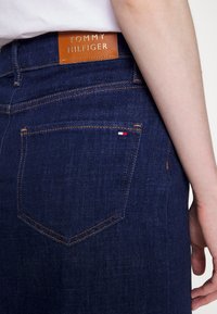 Tmavě modré džínové kalhoty s měděným šitím a koženou štítkem na pásku. Na zadním kapse je malý detail s logem.