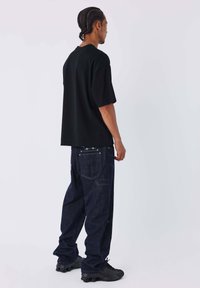 Black oversized T-shirt, dark blue jeans with stitching details, and black sneakers. Smooth fabric and relaxed fit. Simple design.