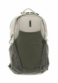 Zaino Thule di colore grigio chiaro con una sezione inferiore verde testurizzata. Presenta cerniere, tasche laterali e una maniglia di trasporto superiore.