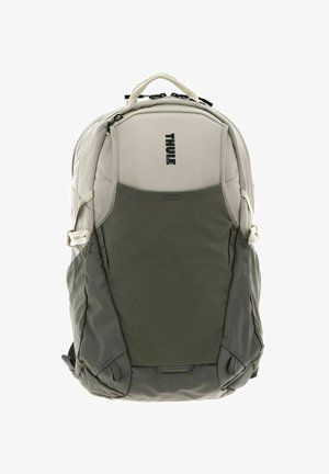 Thule backpack in light gray with a textured green lower section. Features zippers, side pockets, and a top carry handle.
