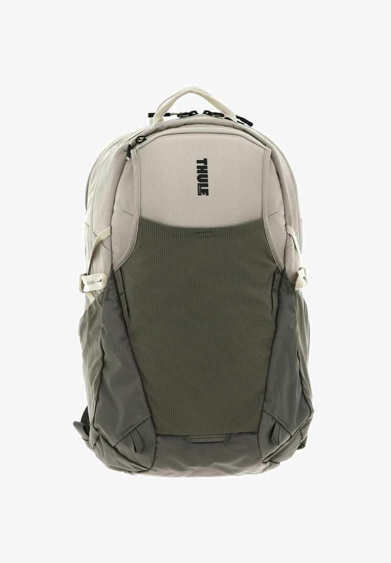 Mochila Thule en gris claro con una sección inferior texturizada en verde. Cuenta con cremalleras, bolsillos laterales y un asa superior.