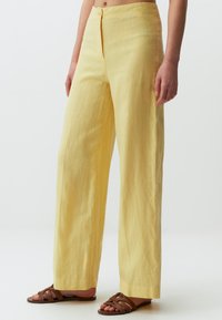Gele linnen wijde broek met een zachte textuur, sluiting met een voorste knoop en zijvakken. Gemaakt met bruine sandaaltjes met banden.