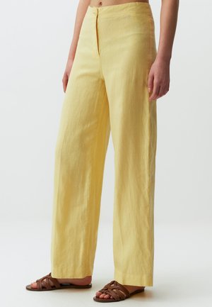 Gele linnen wijde broek met een zachte textuur, sluiting met een voorste knoop en zijvakken. Gemaakt met bruine sandaaltjes met banden.