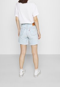 Pantalones cortos de mezclilla azul claro con dobladillos deshilachados, cintura alta y bolsillos traseros. Combinados con zapatillas blancas y una camiseta blanca de corte holgado.