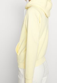 Gul huva sweatshirt i mjukt material, har en kenguruficka, ribbade muddar och nederkant, med vita dragskor för justering.