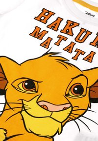 Lähikuva Simban kasvoista Leijonakuningas-elokuvasta, jossa ylhäällä on boldilla oranssilla tekstillä "Hakuna Matata" valkoisella kankaalla.