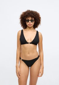Μαύρο μπικίνι με ραβδώσεις, που διαθέτει τοπ με βαθύ V και φαρδιές τιράντες, συνοδευόμενο από μπικίνι με χαμηλή μέση.