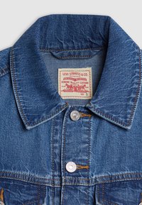 Col de veste en denim bleu Levi's avec deux boutons argentés et une étiquette blanche indiquant la marque et la taille small.