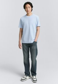 Tricou scurt, de culoare albastru deschis, purtat cu blugi de culoare albastru închis. Tricoul are un guler rotund. Încălțăminte casual albă și neagră.