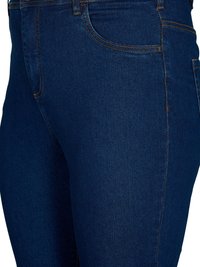 Jeans de mezclilla azul oscuro con corte slim, con costuras naranjas, bolsillos frontales y una textura suave. Diseño clásico de cinco bolsillos.