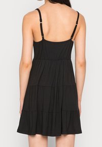 Svart ärmlös klänning med justerbara band, laget i flera lager och mjukt material. Har en figurnära liv och utsvängd nederkant.