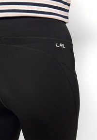 Leggings pretos com uma textura suave, apresentando uma costura curva e um logo "LRL" branco na cintura. Design simples e funcional.