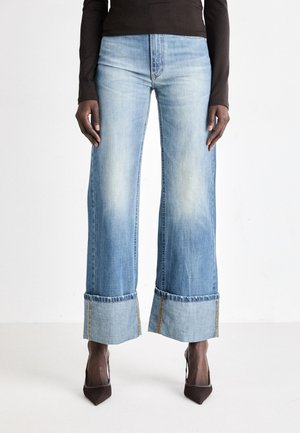 Light blue wide-leg jeans with a faded wash, featuring rolled cuffs and contrasting stitching. Paired with dark high-heeled shoes.
