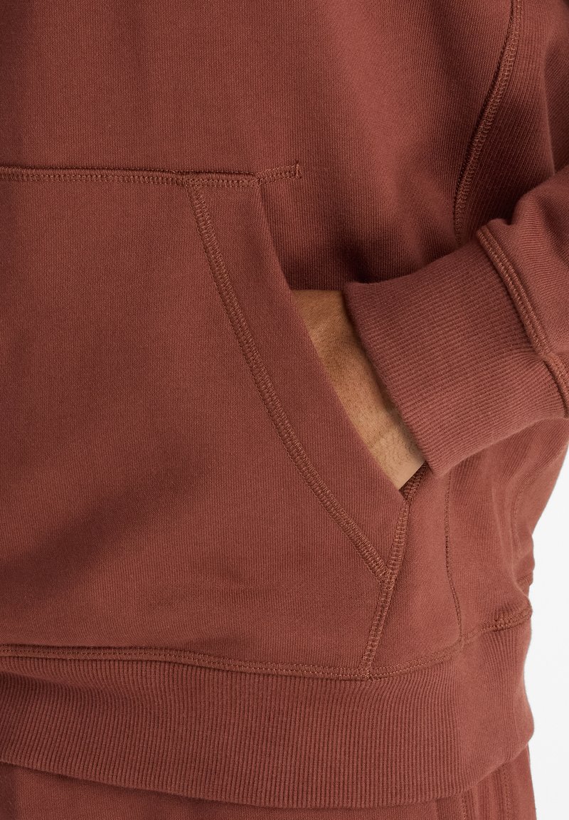 Maroon sweatshirt with a hand in the front pocket. Features textured fabric, ribbed cuffs, and a straight hem design.