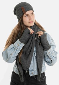 Grijze gebreide beanie, bijpassende sjaal en vingerloze handschoenen. Zachte textuur met ribbel- en wafelpatronen. Spijkerjack met opgerolde mouwen.