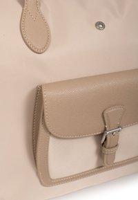 Borsa a spalla beige con tasca frontale in pelle strutturata, corpo in tessuto liscio, hardware in argento e dettagli di cucitura a contrasto.