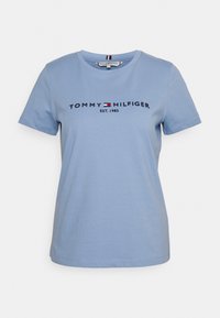 T-shirt in cotone azzurro chiaro a maniche corte con "Tommy Hilfiger EST. 1985" e un piccolo logo rosso, bianco e blu sul petto.