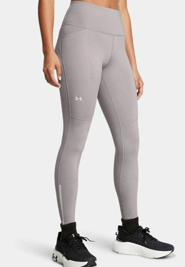 Leggings de sport gris avec une taille haute, des détails de couture et un logo sur la jambe inférieure. Portés avec des chaussures de sport noires.