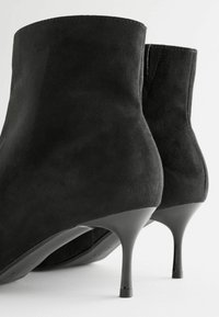 Mustat mokkanahkaiset nilkkurit, joissa on sileä pinta, kapeneva siluetti ja stilettikorko. Minimalistinen ompelu ja klassinen muotoilu.