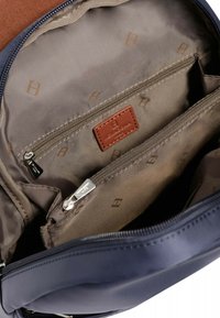 Interno di una borsa navy con etichetta in pelle marrone, fodera beige e più scomparti. Presenta due tasche con zip e una texture liscia.