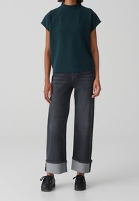 Top verde acqua con collo a imbuto e maniche corte abbinato a jeans grigio scuro a vita alta, a gamba larga, con orli risvoltati e scarpe nere.