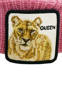 Tessuto lavorato a maglia rosa con un patch ricamato che presenta il volto di un leone e la parola "QUEEN" in testo nero su uno sfondo bianco.