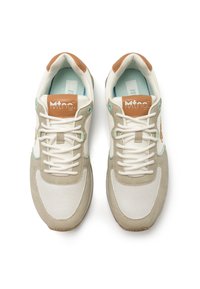Zapatillas beige y blancas que combinan materiales de ante y malla, con cordones redondos, un parche de logo marrón y detalles en color azul verdoso. Suela de goma plana.