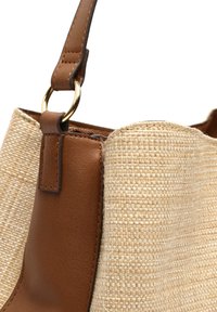Cintura in pelle color tan con un anello in metallo dorato attaccato a una borsa di paglia intrecciata. La borsa presenta una superficie intrecciata di un beige chiaro e texturizzato.