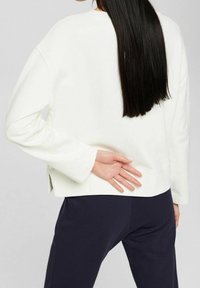 Witte katoenen sweatshirt met lange mouwen, lichte zijinsneden, geribbelde manchetten en een ontspannen pasvorm. Gecombineerd met marineblauwe broek.