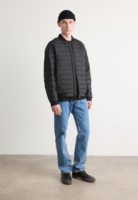 Doudoune noire avec fermeture éclair sur le devant, texture matelassée et poignets côtelés. Assorti à un jean bleu clair et des baskets noires.