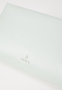Portafoglio in pelle testurizzata blu chiaro con logo "FURLA" in rilievo nella parte inferiore. Presenta una finitura liscia e un design minimalista.