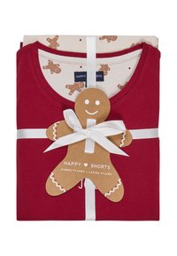 Czerwone bawełniane piżamy starannie złożone z jasnobeżowym topem ozdobionym wzorami pierników, związane białą wstążką z zawieszką w kształcie piernika.
