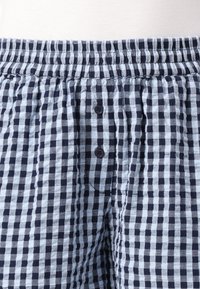 Shorts de pyjama à carreaux pour homme en bleu marine et bleu clair, avec une taille élastique et deux boutons à l'avant. Tissu doux et léger.
