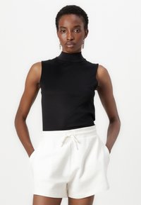 Black sleeveless top with a high neck paired with white drawstring shorts. The fabric is smooth with a relaxed fit.