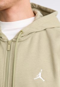 Light green zip-up hoodie made of soft fabric, featuring a white embroidered logo and adjustable drawstrings at the neckline.
